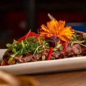 A vibrant gourmet dish topped with microgreens and an edible flower, served on a sleek plate.