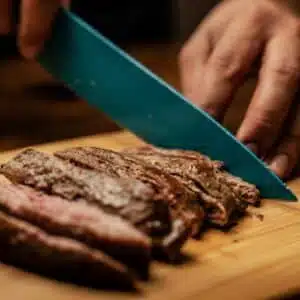 Hands slicing tender, juicy grilled steak on a wooden board, showcasing a mouth-watering culinary scene.